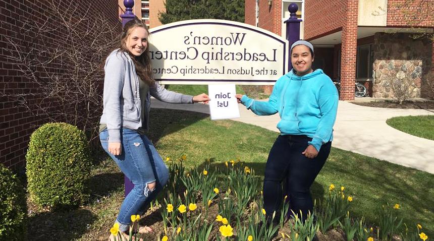 Two ladies posing in front of the Women's leadership sign